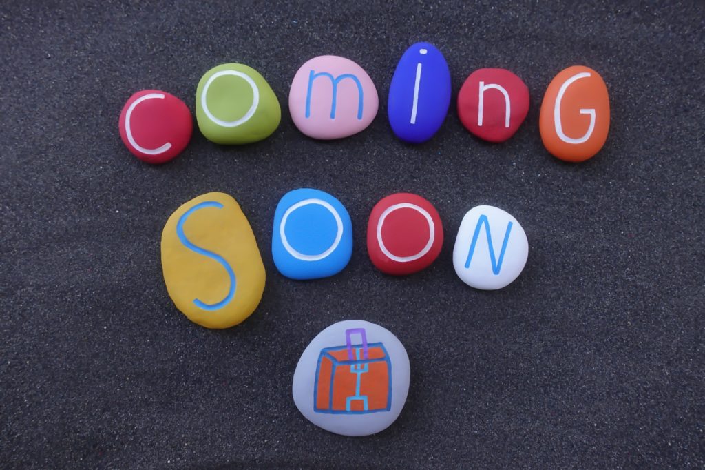 Coming soon text with colored stones design over black volcanic sand
